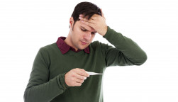 Young man holding his hand to his forehead and holding a thermometer